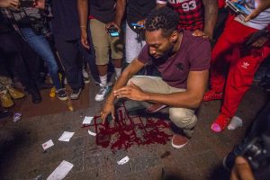 A man crouches over blood left on the sidewalk seconds after a protester on Trade St. was shot in the head and carried off by CMFD and nearby protesters attempting to help him during protests Wednesday evening in uptown Charlotte, NC.